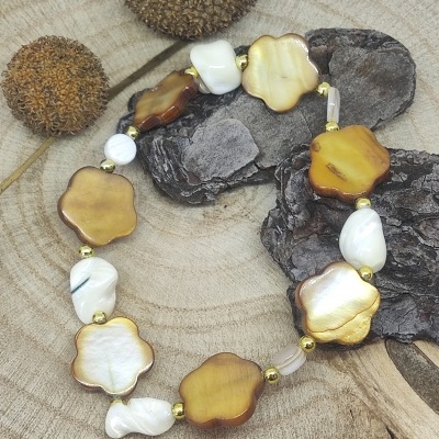 Pulseira de madrepérola em forma de flor com contas douradas sobre base de madeira