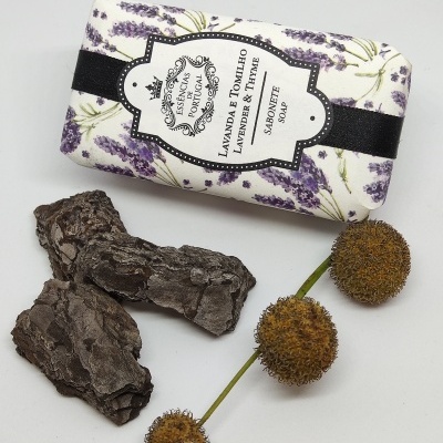 Sabonete com embalagem floral de lavanda, pedaços de casca de árvore escura e três esferas marrons secas em fundo branco