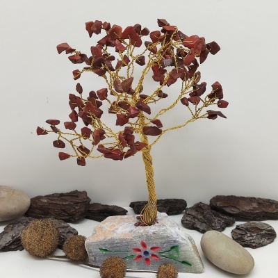 Árvore decorativa de fios dourados com pedras vermelhas numa base de pedra branca pintada com padrão floral.