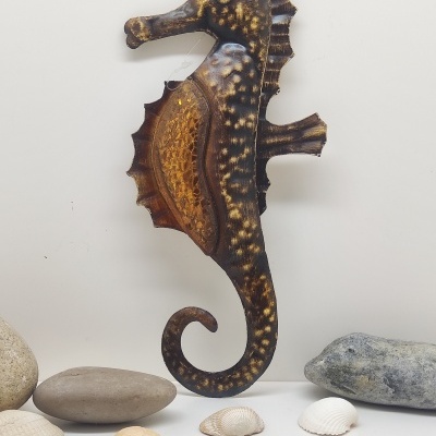 Escultura de cavalo-marinho em metal com pedras e conchas em fundo branco.