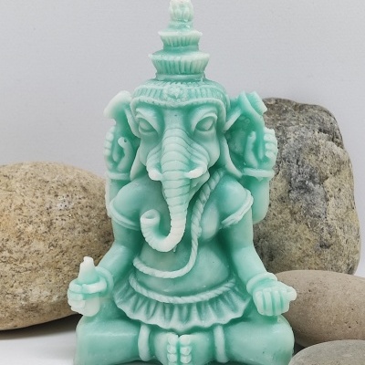 Vela verde em forma de Ganesha sentado com quatro braços e pavio no topo, rodeada por pedras.