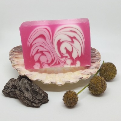 Sabonete marmoreado rosa e branco sobre concha com casca de árvore e flores secas.