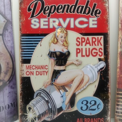 Placa metálica vintage com mulher pin-up e texto publicitário de velas de ignição.