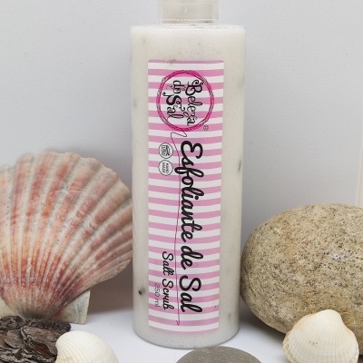 Frasco de esfoliante de sal com rótulo rosa e branco rodeado por conchas e pedras