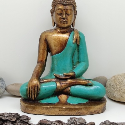 Estátua de Buda dourada e turquesa rodeada de pedras e casca de árvore