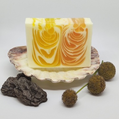 Sabonete artesanal com padrões amarelo e laranja numa concha com casca de árvore e bolbos secos