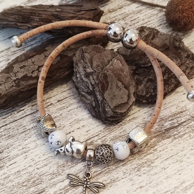 Pulseira de cortiça bege com contas decorativas e pingente de libélula sobre madeira clara