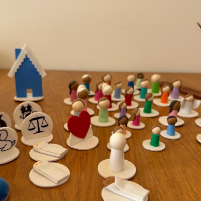 Peças de jogo de madeira coloridas em forma de pessoas e símbolos, dispostas sobre mesa de madeira