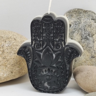 Vela em forma de mão de Hamsá com padrões detalhados e pedras ao redor