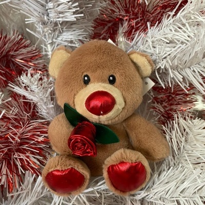 Ursinho de pelúcia castanho claro com nariz e patas vermelhos em fundo de ramos brancos e vermelhos