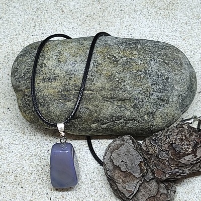 Colar com pendente de pedra azul translúcida e cordão preto sobre pedra e cascas