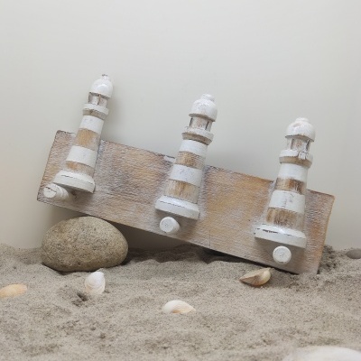 Três ganchos decorativos de madeira branca com efeito envelhecido sobre base de madeira na areia