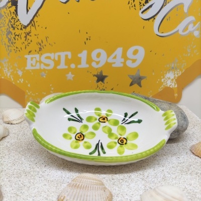 Prato oval de cerâmica decorado com flores verdes, sobre mesa areia com conchas e fundo amarelo com texto