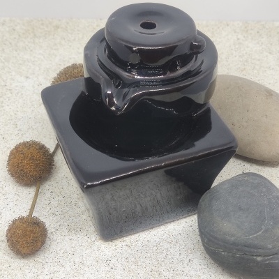 Frasco de vidro preto quadrado com tampa redonda junto a pedras e frutos secos.