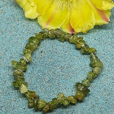 Bracelete de pedras verdes sobre superfície azul com flor amarela