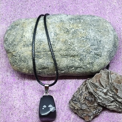 Colar com pendente preto e branco sobre pedra cinzenta e fundo rosa