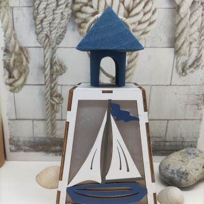 Lanterna decorativa de madeira com barco e casa azul em fundo com cordas e pedras