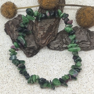 Pulseira de pedras verdes e roxas sobre cascas de árvore com flores secas.