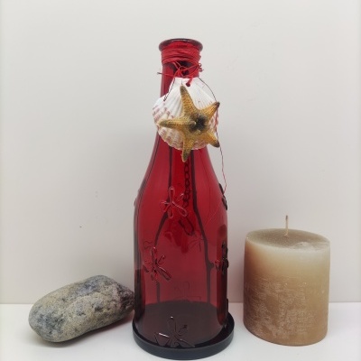 Garrafa decorativa vermelha com enfeites marinhos, vela castanha e pedra cinzenta