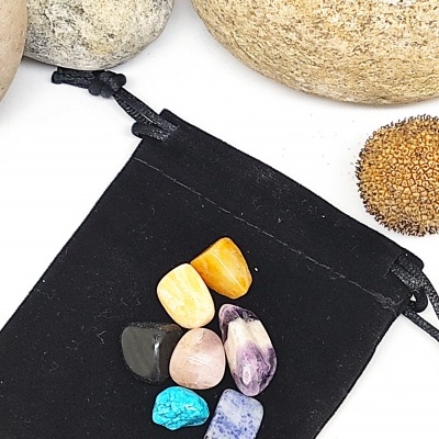 Sete pedras polidas variadas sobre saco de tecido preto com pedras naturais ao redor