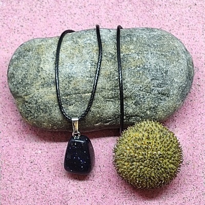 Colar com pendente de pedra preta sobre pedra cinzenta e fruto espinhento em fundo rosa.