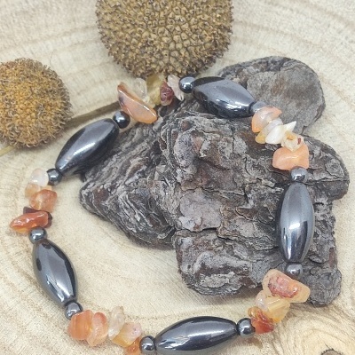 Pulseira com contas pretas e pedras laranja sobre casca de árvore