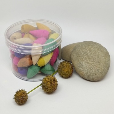 Frasco com cones de incenso coloridos, duas pedras cinzentas e galho com bolinhas secas