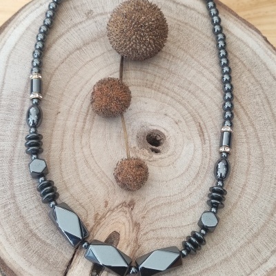 Colar preto brilhante de contas variadas sobre base de madeira circular com frutos secos marrons