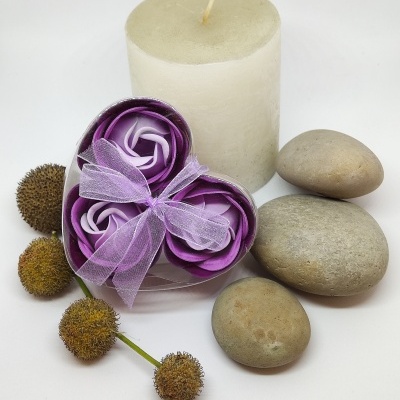 Conjunto decorativo com vela, pedras, frutos secos e flores de tecido roxo em caixa transparente em forma de coração.