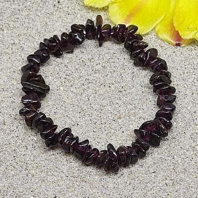 Pulseira de pedras grená escuras sobre superfície cinza com flor amarela ao lado