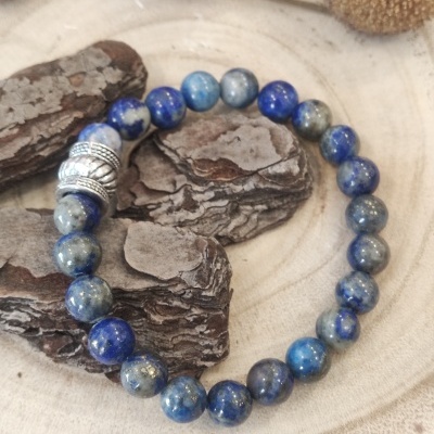 pulseira de contas azuis com separador metálico sobre fundo de madeira e casca