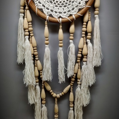 Apanhador de sonhos em madeira e croché branco com franjas e contas penduradas.