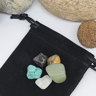 Cinco pedras coloridas polidas sobre saco preto de tecido com pedras maiores ao fundo