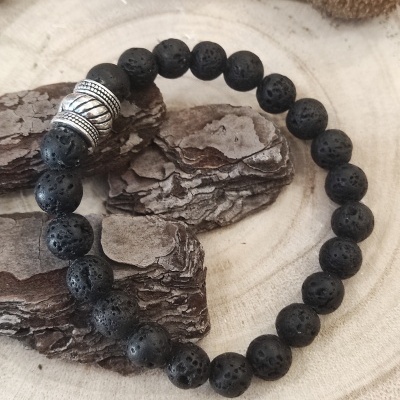 Pulseira de contas pretas porosas e conta prateada sobre superfície de madeira clara