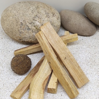 Pedaços de madeira claros empilhados sobre areia com pedras cinzentas e uma bola marrom