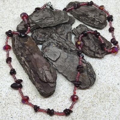 Colar de contas vermelhas e pedras escuras sobre casca de árvore sobre superfície clara