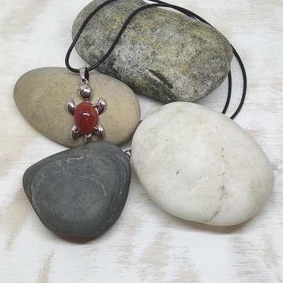 Colar com pendente de tartaruga em pedra vermelha e metal prateado, cordão preto, sobre pedras decorativas