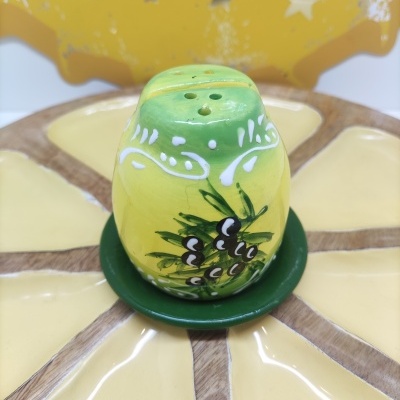 Saleiro cerâmico verde e amarelo com decoração de pinhas, sobre prato com padrão amarelo e castanho, com letreiro amarelo ao fundo