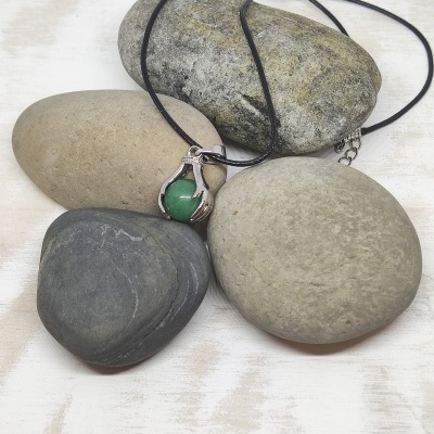 Colar com pendente de pedra verde e moldura em forma de mão sobre pedras lisas