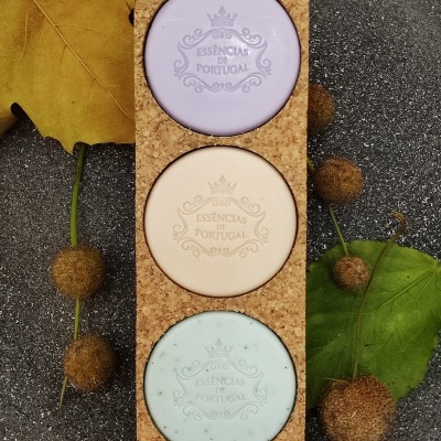 Três sabonetes coloridos em suporte de cortiça com folhas e bolotas ao redor