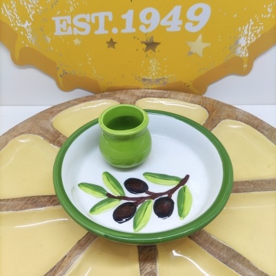 Prato de cerâmica com padrão de azeitonas e vaso verde sobre base decorativa amarela