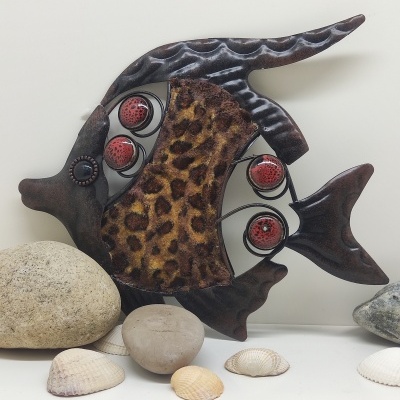 Escultura de peixe em metal e tecido com padrão de pele de leopardo sobre superfície branca com conchas e pedras