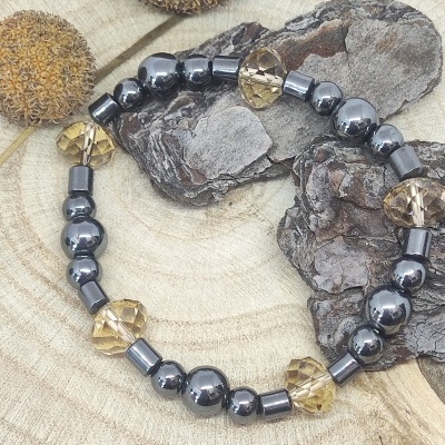 Pulseira com contas metálicas cinza escuro e âmbar sobre fundo de madeira com cascas e frutos secos