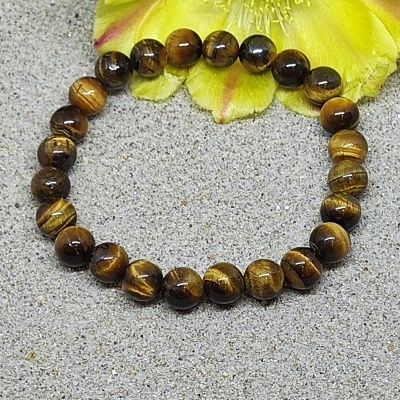 Pulseira de contas de pedra olho de tigre castanha com reflexos dourados sobre superfície cinzenta e flor amarela