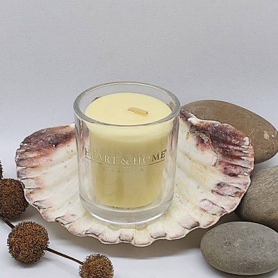 Vela amarela em copo de vidro com inscrição Heart & Home sobre concha grande com pedras e flores secas ao lado