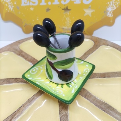 Conjunto de jarro e prato cerâmicos com espetos metálicos com cabos pretos, sobre prato redondo dividido, fundo com placa amarela EST.1949