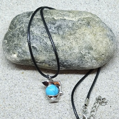 Colar com pendente prateado e pedra azul sobre pedra cinzenta e areia