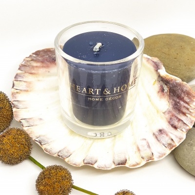 Vela azul em copo de vidro sobre concha com flores secas e pedras