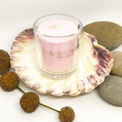 Vela rosa em copo de vidro sobre concha grande com pedras e flores secas