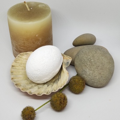 Conjunto com vela bege, sabonete branco em concha, pedras cinzentas e bolinhas castanhas